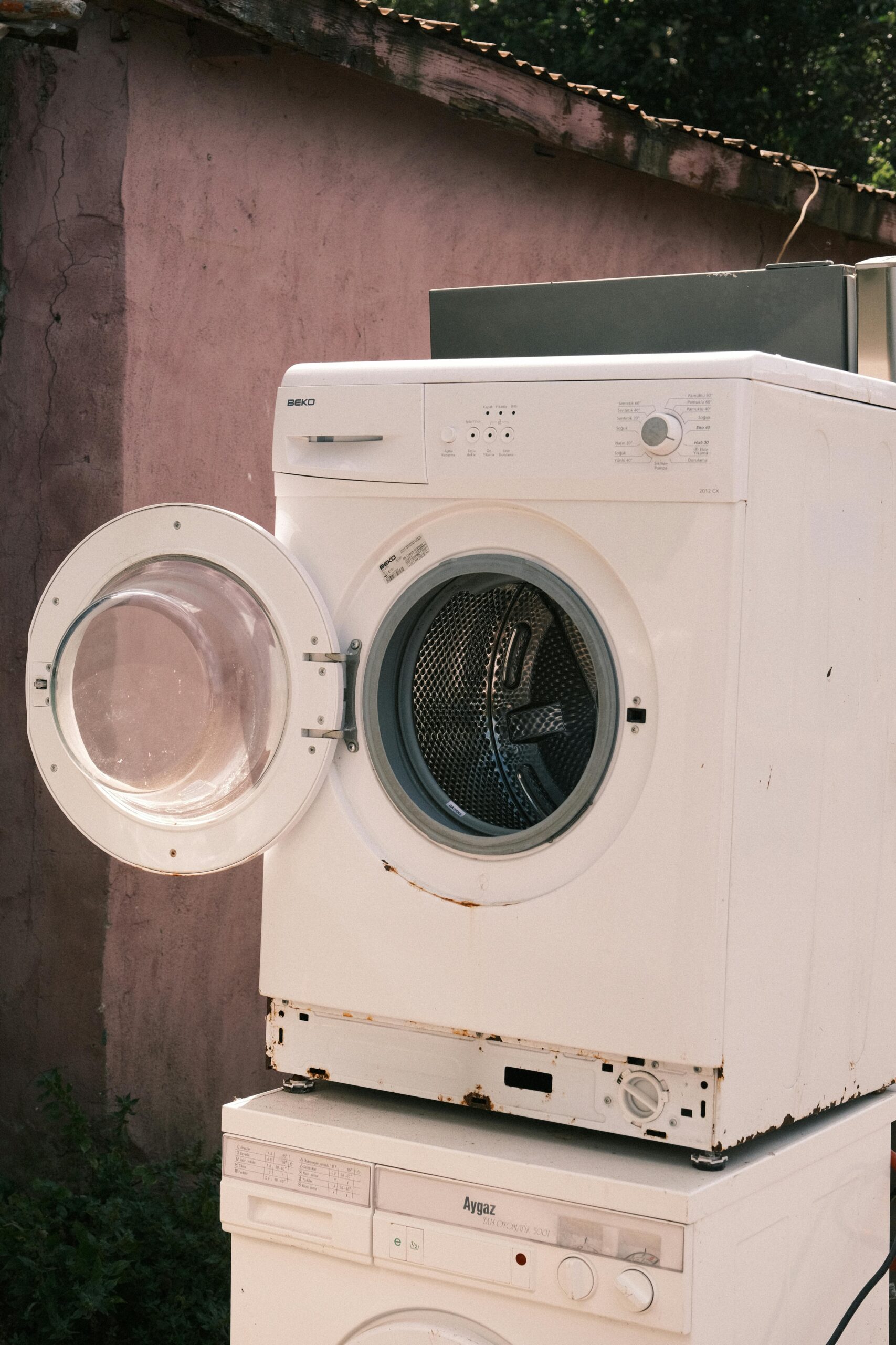 Outdoor view of two stacked laundry machines with an open door, showing rustic surroundings.