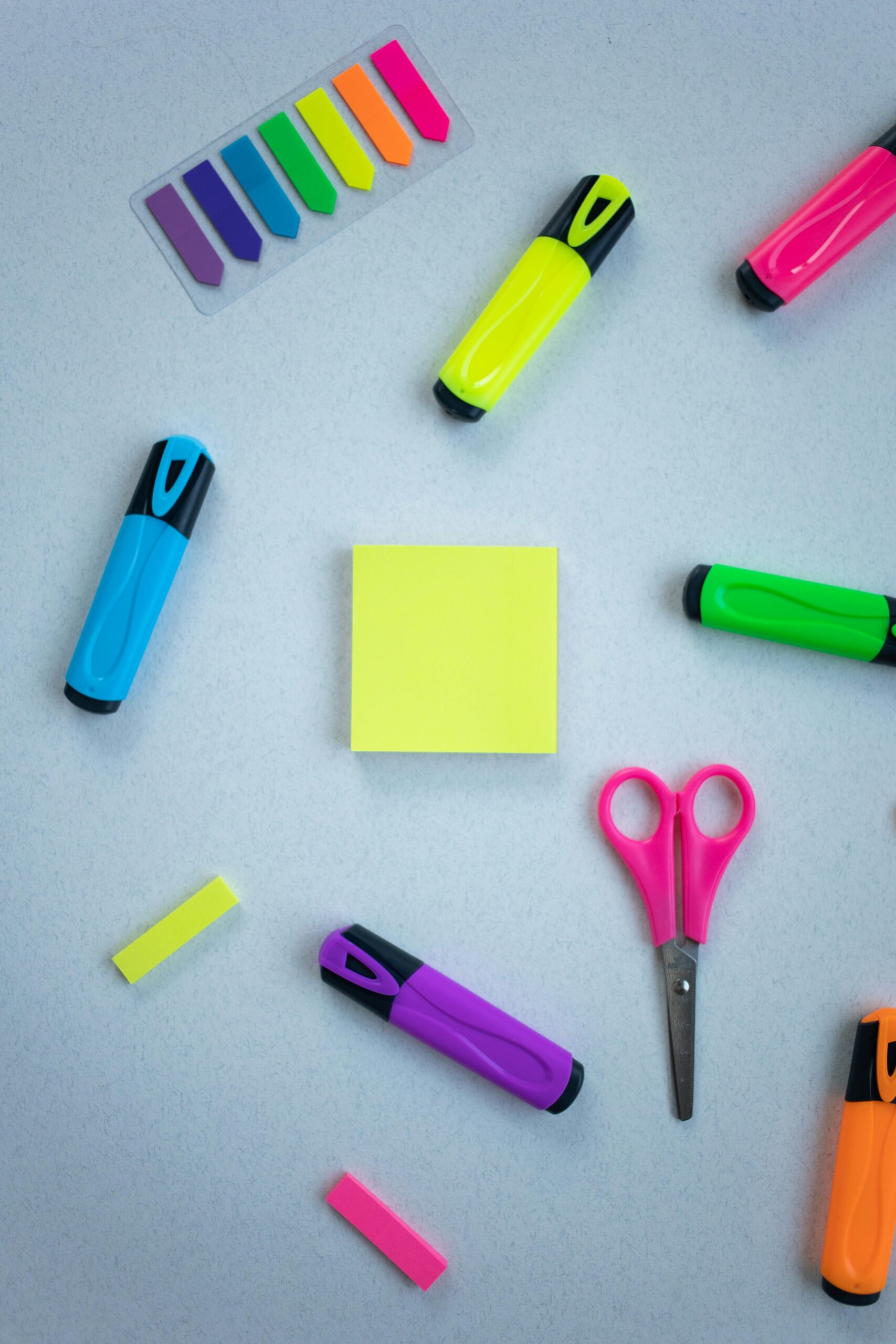 Vibrant stationery flat lay featuring colorful highlighters, sticky notes, and scissors on a white background.